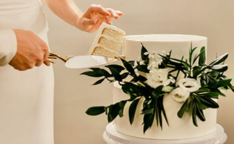 wedding cake being cut with bride receiving a slice on a plate